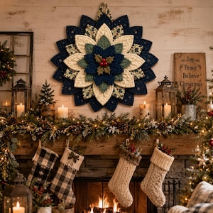 May include: A circular fabric wall hanging featuring a layered poinsettia design in navy blue, cream, and green with a central cluster of red berries. The quilted petals are arranged in a starburst pattern with a small hanging loop at the top.