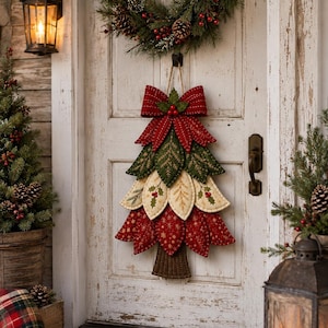 May include: A fabric Christmas tree wall hanging featuring layered, quilted leaf-shaped segments in red, cream, and green with gold stitching. The tree is topped with a large red fabric bow and has a brown fabric trunk at the base, hanging by twine.