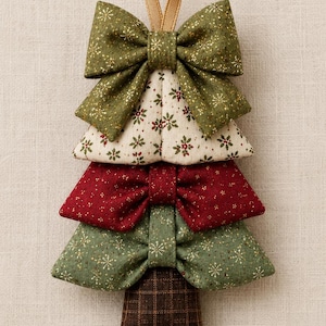 May include: A decorative Christmas tree ornament constructed from stacked fabric bows. The top bow is olive green with gold glitter, followed by a cream section with red and green floral patterns, a deep red bow, a green bow, and a brown plaid base.