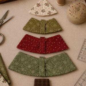 May include: A set of fabric pieces arranged to form a Christmas tree shape, including a cream triangular top with red and green floral patterns, two green trapezoidal sections with snowflake prints, a red trapezoidal section, and a brown plaid base.