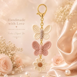May include: A gold-toned metal keychain featuring two crocheted butterflies and one crocheted flower. The top butterfly is cream, the middle butterfly is dusty pink, and the bottom flower is cream with a brown center. Text reads: Handmade with Love.