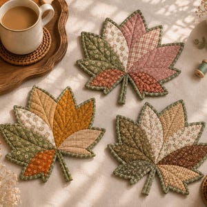 Puede incluir: Tres posavasos de tela acolchada con forma de hojas de arce, con dise&ntilde;os de patchwork en colores oto&ntilde;ales que incluyen verdes apagados, rosas empolvados, naranjas c&aacute;lidos y marrones, con costuras detalladas en la superficie de cada hoja.