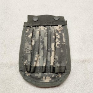 Könnte beinhalten: Eine taktische Tasche mit digitalem Tarnmuster in Olivgrün, Beige und Dunkelgrau. Die Tasche hat einen einfarbigen olivgrünen Rand, eine verstärkte obere Klappe mit zwei Druckknöpfen und drei vertikale elastische Fächer zur Aufbewahrung.