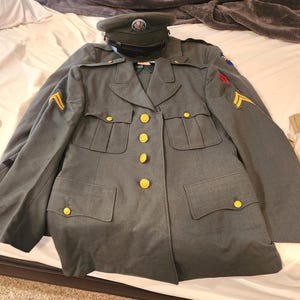 May include: An olive drab military service uniform jacket featuring gold-toned buttons, four front pockets, and yellow chevron rank insignia on the sleeves. A matching olive drab service cap with a central emblem is positioned at the top of the jacket.