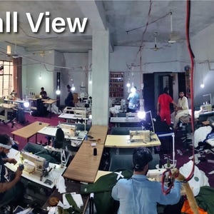 Peut inclure: Une vue panoramique d'un atelier de confection textile avec plusieurs postes de couture équipés de machines industrielles, des éclairages suspendus et des ouvriers. Le texte "Hall View" apparaît dans le coin supérieur gauche.