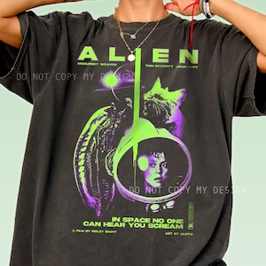 Könnte beinhalten: Ein anthrazitfarbenes Kurzarm-T-Shirt mit einem Grafikdruck zum Film Alien. Das Design zeigt ein Porträt einer Figur in einem Weltraumhelm, eine Kreatur sowie den Text Alien, In Space No One Can Hear You Scream.
