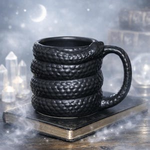 May include: A matte black ceramic mug shaped like a coiled snake. The body of the mug features a textured, scaly surface that wraps around the entire vessel, with the snake's head forming the top of the handle and its tail curving at the base.