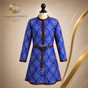Puede incluir: Una túnica de manga larga en azul vibrante con un patrón circular repetitivo y detalles geométricos en blanco y rojo. La prenda incluye una tapeta de botones marrón, un cuello marrón y un cinturón marrón a juego en la cintura.