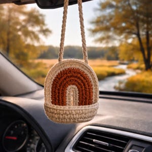 Autohanger in de vorm van een boog in gebrande sienna, minimalistisch gehaakt met punch needle-techniek, ideaal voor de achteruitkijkspiegel.