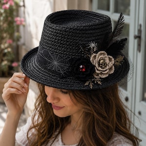 May include: A black woven straw fedora hat featuring a black ribbon band with a white spiderweb pattern. The hat is decorated with a black crocheted flower with a red center, a beige crocheted flower with a small skull, black feathers, and netting.