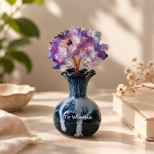 May include: A decorative tree sculpture made of purple and clear crystal chips on copper wire branches, set in a small, round, dark blue and white glazed ceramic vase with the text To Winnie printed on the front in white script lettering.