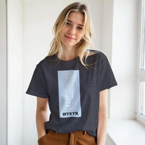 May include: A dark charcoal gray short-sleeve t-shirt featuring a vertical light blue rectangular graphic on the chest. The graphic contains four white line-art symbols stacked vertically above the black text #IYKYK printed in a bold sans-serif font.
