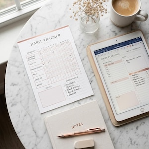 Peut inclure: Un suivi d'habitudes en papier blanc avec des accents en or rose, une tablette affichant une interface de planification quotidienne, un carnet beige marqué NOTES et un stylo en or rose. Le suivi inclut des lignes pour la routine matinale.