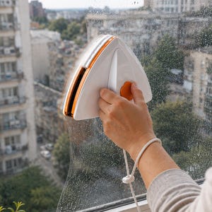 Può includere: Un pulitore magnetico per vetri di forma triangolare con esterno in plastica bianca, dettagli arancioni e un cordino di sicurezza. Il dispositivo è posizionato su una lastra di vetro e presenta due sezioni collegate per la pulizia simultanea.