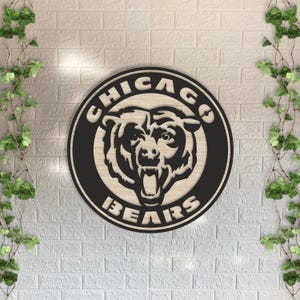 Può includere: Un'insegna da parete circolare in legno con il logo dei Chicago Bears. Il design presenta al centro la sagoma nera di una testa di orso con la bocca aperta, circondata da un bordo circolare nero contenente la scritta CHICAGO BEARS in bianco.