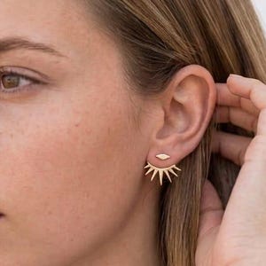 May include: A gold-toned ear jacket earring featuring a small marquise-shaped stud at the front and a fan-shaped sunburst design that extends below the earlobe. The piece is crafted with a polished metallic finish and a secure post-back closure.