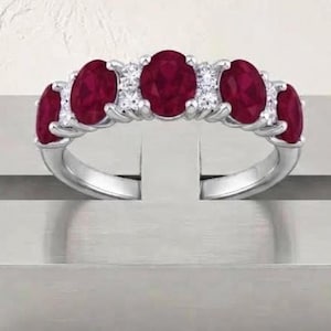 May include: A silver-toned ring featuring five oval-cut deep red rubies arranged in a row, interspersed with four small, clear, round-cut white stones set in a prong setting along the top band of the jewelry piece.