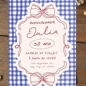 May include: A rectangular invitation card featuring a blue and white gingham pattern background. A cream-colored central label with red ribbon illustrations at the top and bottom contains the text: Anniversaire Julia 30 ans SAMEDI 27 JUILLET À partir de 15H00 123 anywhere st., any city, st 12345.