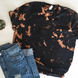 以下が含まれることがあります： 茶色のブリーチタイダイ柄の黒いTシャツ。Vネックと半袖です。