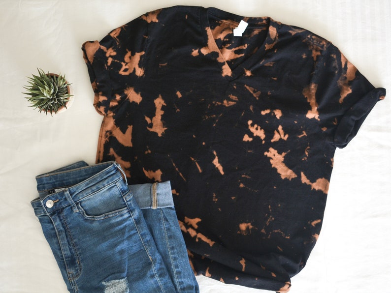 以下が含まれることがあります： 茶色のブリーチタイダイ柄の黒いTシャツ。Vネックと半袖です。