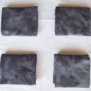 May include: Four folded gray fabric squares with a tie-dye pattern. The fabric has a dark gray color with lighter gray spots.