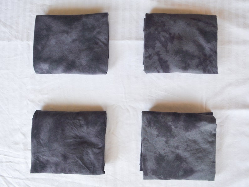 May include: Four folded gray fabric squares with a tie-dye pattern. The fabric has a dark gray color with lighter gray spots.