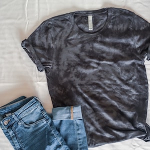 May include: A dark gray tie-dye t-shirt with rolled up sleeves and a pair of blue jeans.
