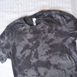 May include: A black tie-dye t-shirt with a round neckline. The shirt has a faded, abstract pattern.