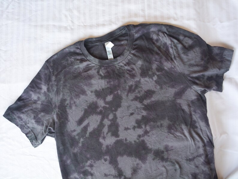 May include: A black tie-dye t-shirt with a round neckline. The shirt has a faded, abstract pattern.