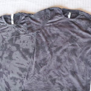 May include: Two gray tie-dye t-shirts with a crew neck and short sleeves.