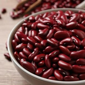 May include: A round, light-colored bowl filled to the brim with dried dark red kidney beans. The beans have a smooth, shiny surface and a distinct kidney shape, with a small white hilum visible on the inner curve of many individual beans.
