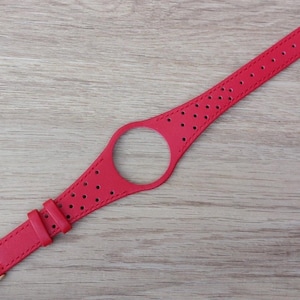 May include: A bright red leather watch strap featuring a circular cutout in the centre for a watch face. The strap has a perforated design with small holes throughout the band, two matching red leather keepers, and a gold-toned metal buckle.