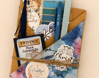 May include: A brown paper envelope containing a reading log, blue sticky notes, a blue pen, a blue highlighter, a Twinings Pure Camomile tea bag, a dark blue tassel, and various stickers with text including "I CAN DO ALL THINGS THROUGH Christ".