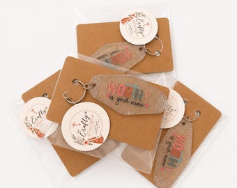 May include: A collection of motel-style keychains in clear plastic packaging on brown cardstock. Each keychain features a glittery tan finish with the text "WORTHY is your name" in multi-coloured letters and a small heart, attached to a metal ring.