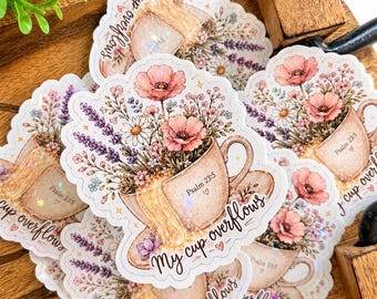 May include: A collection of die-cut stickers featuring a tan teacup overflowing with pink poppies, lavender, and white daisies. The text "My cup overflows" is written in black script, and "Psalm 23:5" with a small heart is printed on the cup.