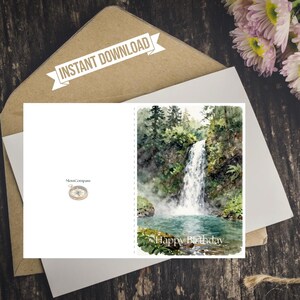 Op de afbeelding: Een gevouwen wenskaart met een aquarelillustratie van een waterval die in een poel stroomt, omringd door bosbomen. De tekst "Happy Birthday" staat onderaan gedrukt, samen met het logo "MossCompass" en een icoon van een kompas.