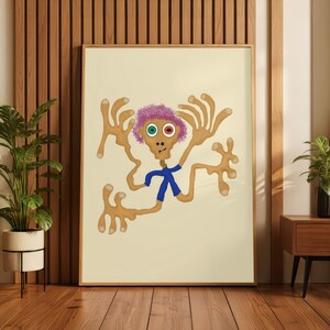 May include: A framed wall art print featuring a tan, multi-limbed creature with a pink, curly-haired head, one green eye, one orange eye, and a small blue shirt. The creature is centred on a light cream background within a wooden frame.