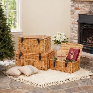 May include: Three rectangular woven wicker storage baskets with hinged lids and dark brown leather-like straps. Two baskets are stacked vertically, while the third sits open to the right, containing a wrapped gift and a small decorative package.