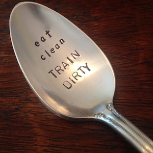 Puede incluir: Una cuchara de plata con las palabras "eat clean train dirty" grabadas.