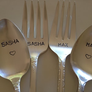 Puede incluir: Dos cucharas de plata y un tenedor con los nombres Sasha y Max grabados. Cada pieza de cubertería tiene un pequeño corazón grabado al lado del nombre.