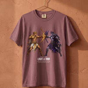 Könnte beinhalten: Ein malvenfarbenes Kurzarm-T-Shirt mit einer Grafik von zwei kämpfenden Figuren, eine in goldener und eine in dunkelvioletter Rüstung. Unter der Grafik steht der Text APOLLO & HADES LIGHT & VOID, gefolgt von kleinerem beschreibendem Text.