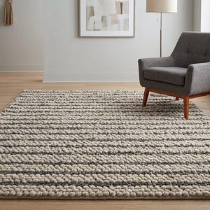 May include: A rectangular area rug featuring a thick, textured, nubby weave in alternating horizontal stripes of cream and dark charcoal gray. The rug has a high-pile, chunky construction that creates a distinct tactile surface pattern across the floor.