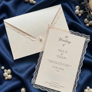 Può includere: Un invito di nozze color crema con busta abbinata, entrambi decorati con un delicato bordo in pizzo. La carta riporta il testo: The Wedding of MELIS & OZAN, 15/06/2026, 19:00, SATO EVENT HALL, ISTANBUL, 34300 BEŞİKTAŞ e altro testo in lingua turca.