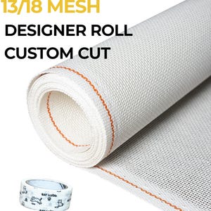 May include: A white needlepoint canvas roll with a 13/18 mesh and an orange guide line, accompanied by a roll of white artist tape featuring black cat and fish illustrations. The text reads 13/18 MESH DESIGNER ROLL CUSTOM CUT and FREE GIFT: ARTIST TAPE.