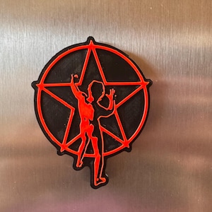 Peut inclure: Un aimant circulaire présentant un motif de pentagramme noir avec un contour rouge vif. Au centre du pentagramme se trouve la silhouette rouge d'une personne avec un bras levé, créant un contraste saisissant avec les éléments noirs.