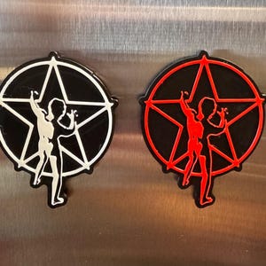 May include: Two circular magnets featuring a black background with a five-pointed star and a silhouette of a person standing inside. One magnet has white outlines and details, while the other magnet has red outlines and details.