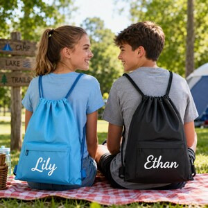Può includere: Due zaini a sacca, uno azzurro con il nome Lily stampato in bianco e uno nero con il nome Ethan stampato in bianco. Entrambe le borse presentano una tasca frontale con cerniera e cordini per essere indossate sulle spalle.