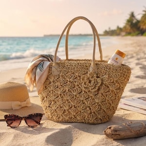 May include: A woven straw tote bag with two light-colored handles, featuring a decorative crochet flower on the front. A patterned scarf is tucked into the side, and a small bottle of sunscreen is placed inside the open top of the bag.