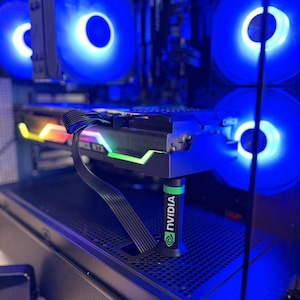 Pode incluir: Uma placa gráfica de computador apoiada por um suporte anti-queda preto e verde da marca NVIDIA dentro de um gabinete de PC. O interior possui várias ventoinhas com iluminação LED azul brilhante e um cabo de alimentação preto conectado.