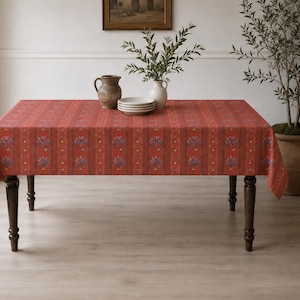 May include: A rectangular tablecloth in a deep red hue featuring vertical stripes and a repeating floral pattern in shades of purple and green. The fabric drapes over a four-legged wooden table, covering the top and sides with a consistent print.